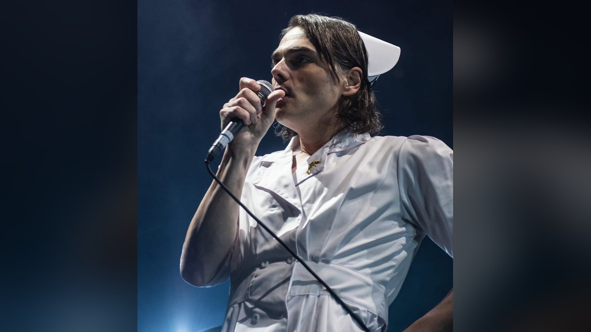 Gerard Way of My Chemical Romance singing into a microphone on stage in a white nurse costume