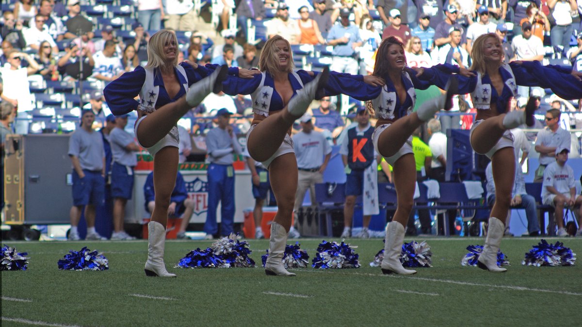 Dallas Cowboys Cheerleaders in their blue and white star uniforms perform a high kick line on the field at a Cowboys home game