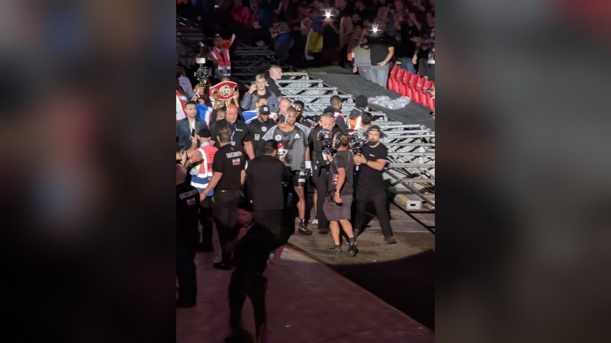 Daniel Dubois walking toward the ring through an arena crowd surrounded by cameramen and his team