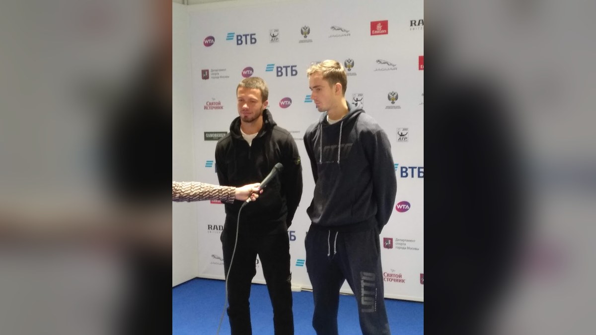 Daniil Medvedev and Evgeny Karlovskiy in dark track jackets standing in front of a sponsor wall at the 2018 Kremlin Cup