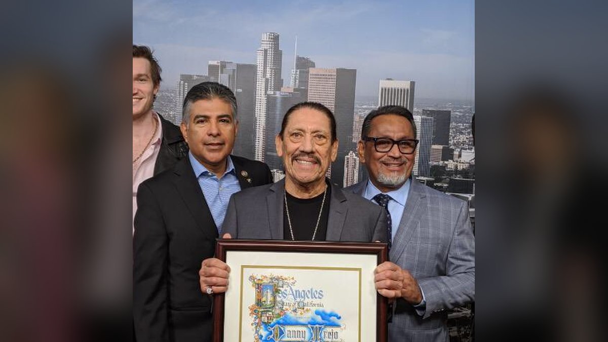 Danny Trejo smiling as he holds a framed Los Angeles city proclamation