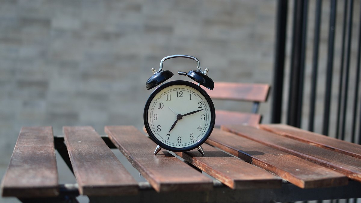 Classic silver alarm clock with a white dial sitting on a wooden patio table