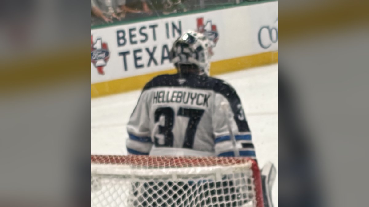 Goaltender Connor Hellebuyck in his white No. 37 Winnipeg Jets jersey and mask standing in the crease during an April 2026 game in Dallas
