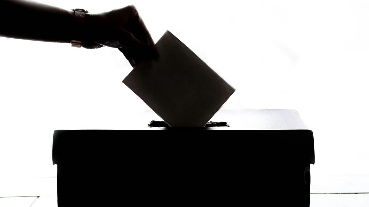 Close view of a person's hand marking a paper election ballot with a blue pen