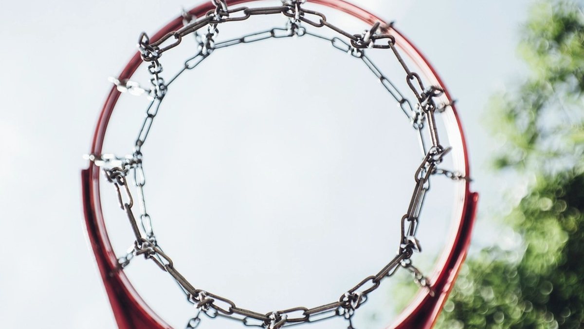 Looking up through a basketball hoop and chain net at the sky