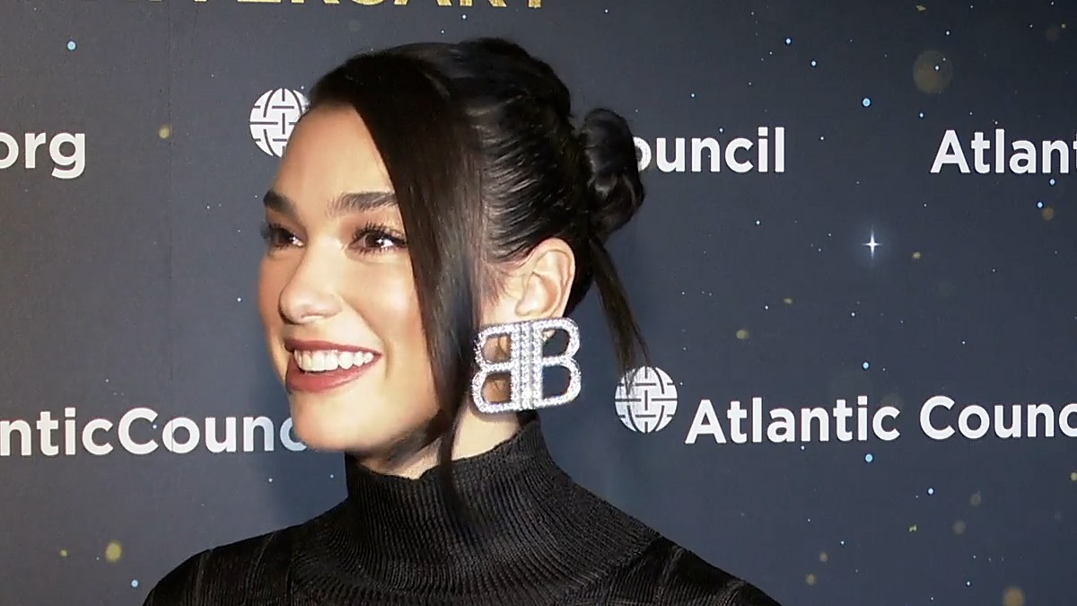 Dua Lipa smiling in a black turtleneck with her hair pulled back
