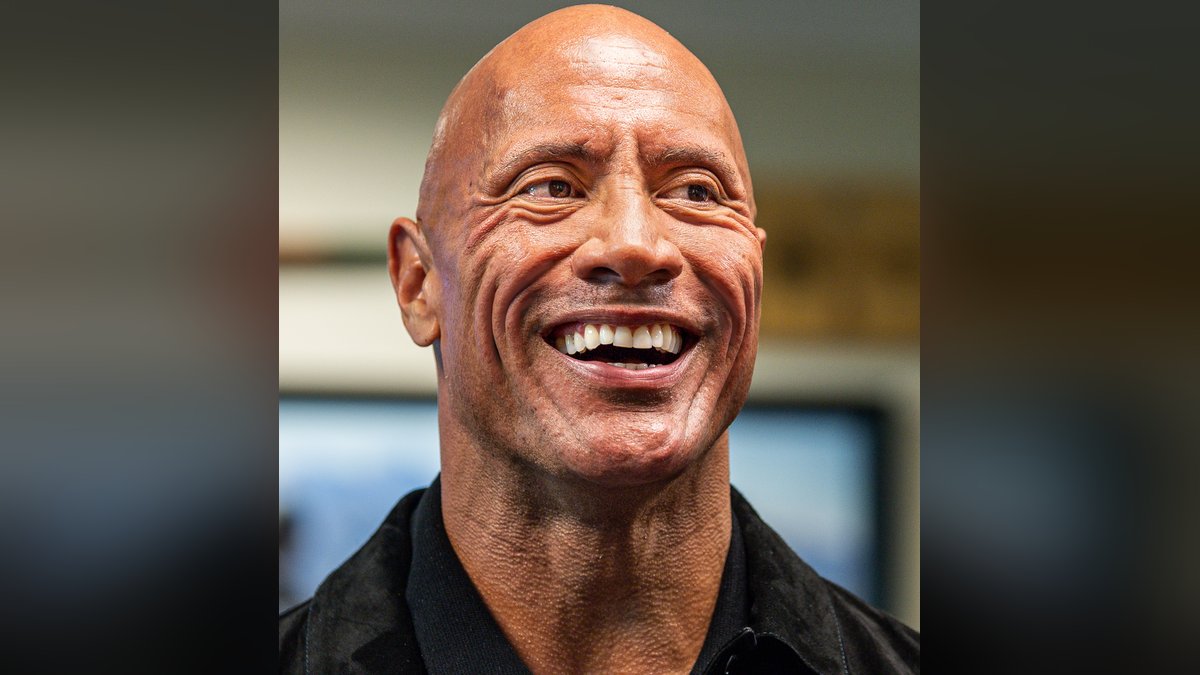 Dwayne Johnson grinning widely in a black shirt and jacket during a visit to the Pentagon