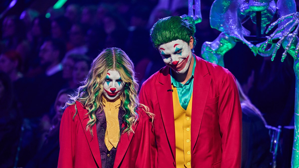 Jackson Olson and Emma Slater in red Joker suits and clown makeup on the Dancing with the Stars ballroom floor during Horror Movie Night