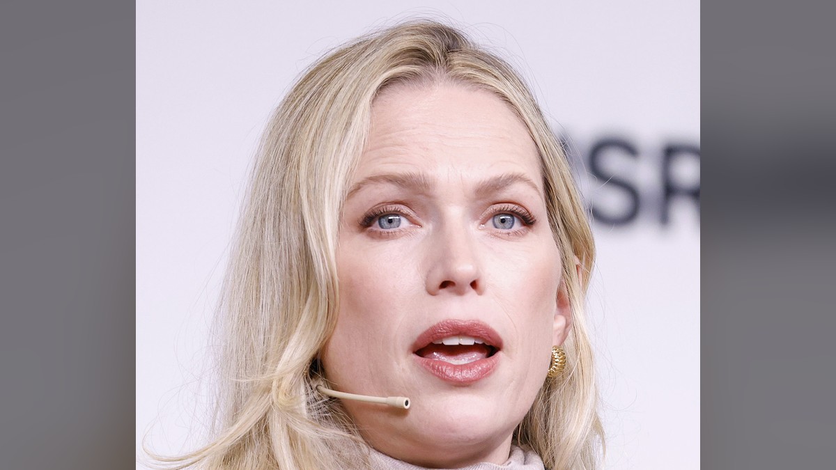 Erin Foster wearing a headset microphone and pinstripe blazer while speaking on stage
