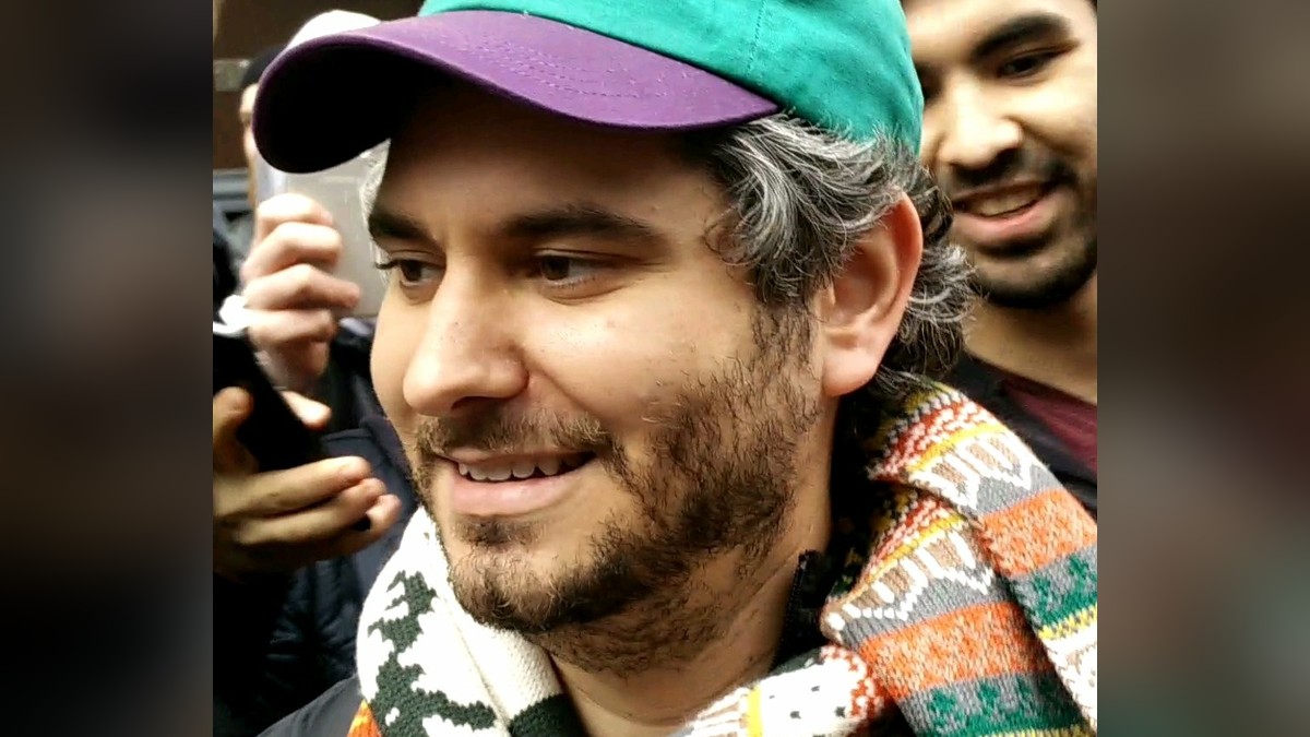 Ethan Klein in a green and purple cap and a patterned scarf surrounded by fans