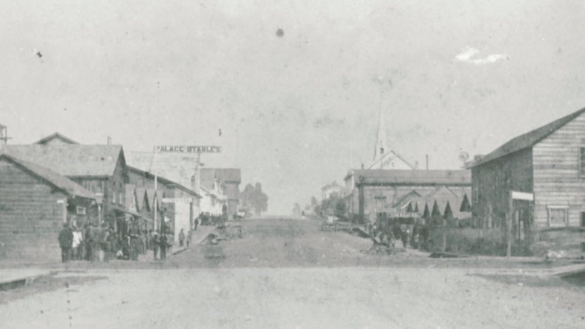 Black and white 1885 photo of a dirt street in Eureka's Chinatown lined with wooden buildings and groups of people