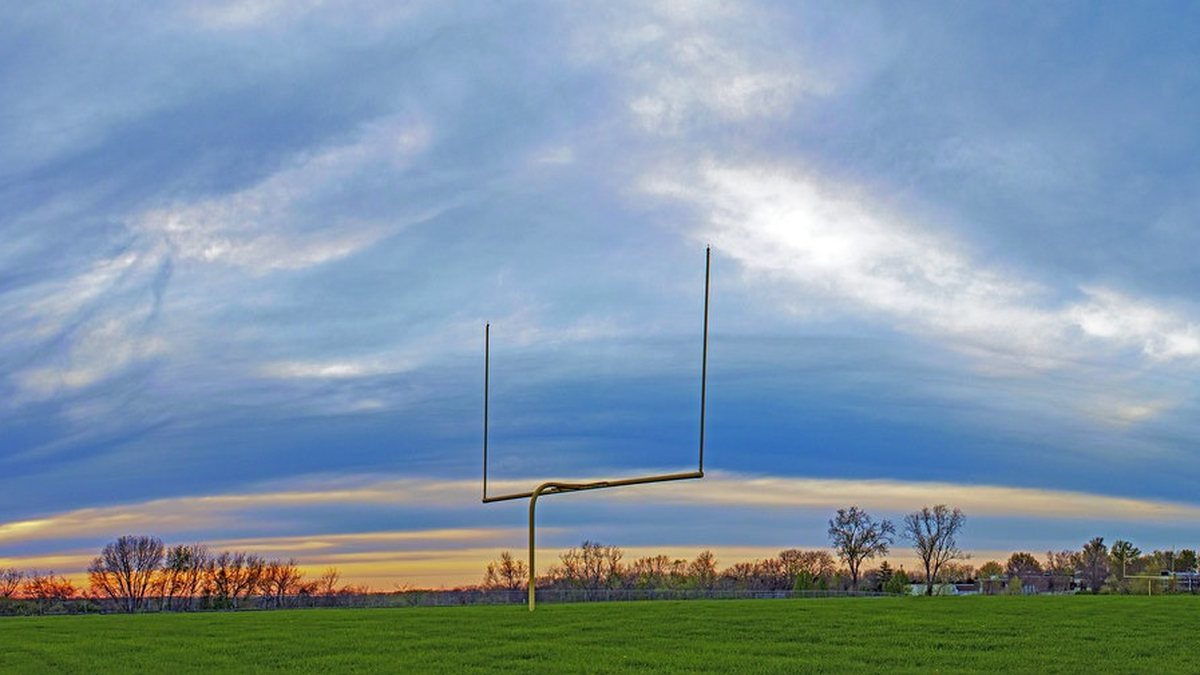 Football goalposts stand over an empty grass field at sunset under a wide streaky sky