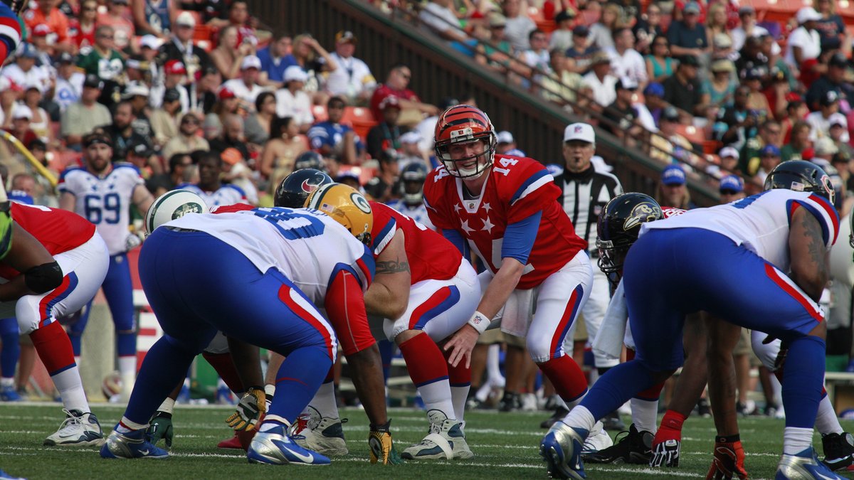 Andy Dalton in a red Pro Bowl jersey with No. 14 and an orange Bengals helmet stands behind his linemen before a snap at the 2012 Pro Bowl in Honolulu