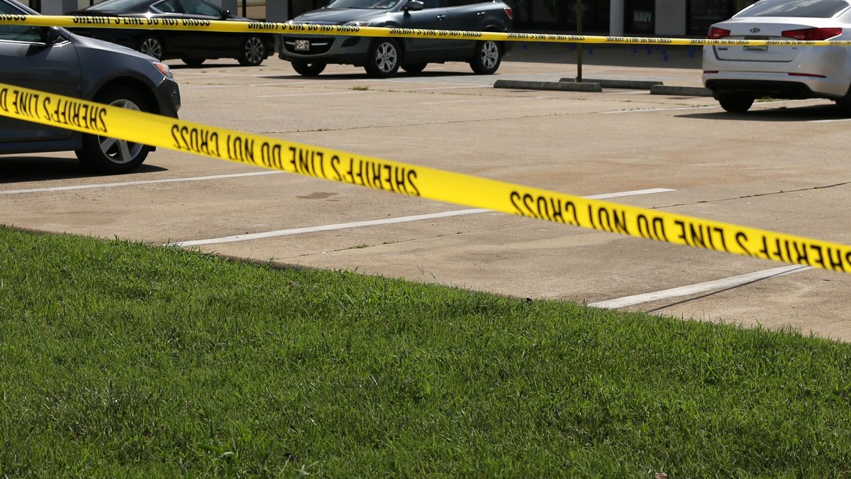 Yellow crime scene tape stretched across a parking lot with cars parked behind it