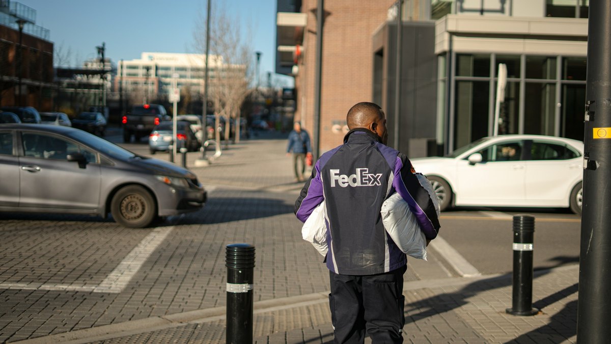 A FedEx courier carrying packages across a sunny downtown street