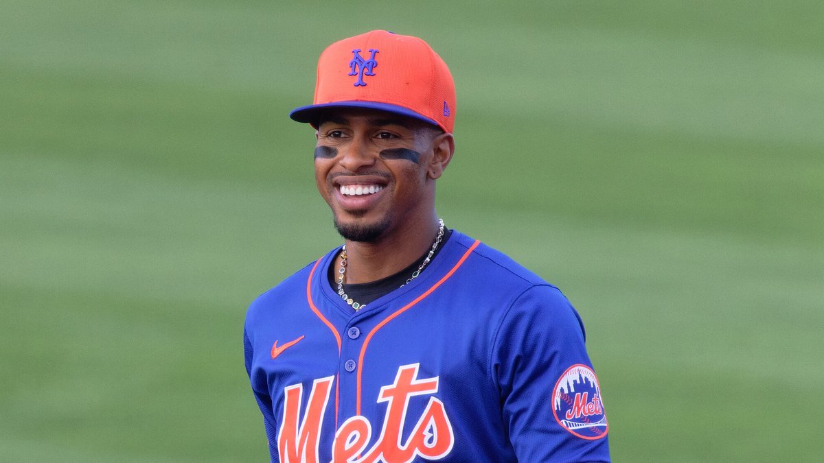 Mets shortstop Francisco Lindor smiling in a blue No. 12 Mets jersey and orange cap on the field