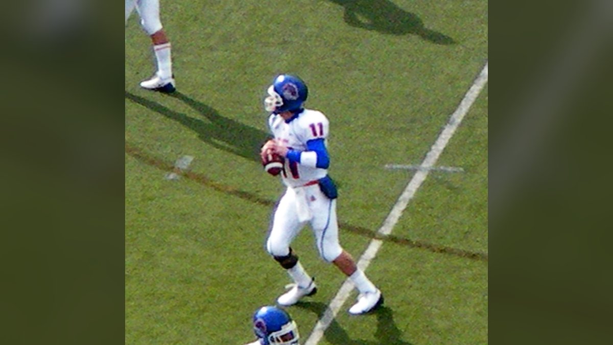 Kellen Moore in a white Boise State No. 11 jersey and blue helmet holds a football during pregame warmups at Nevada in 2008