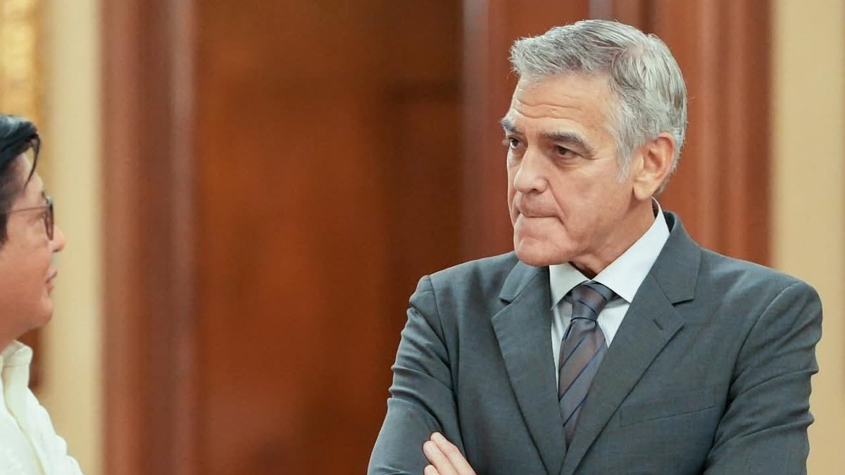 George Clooney in a gray suit standing with his arms crossed