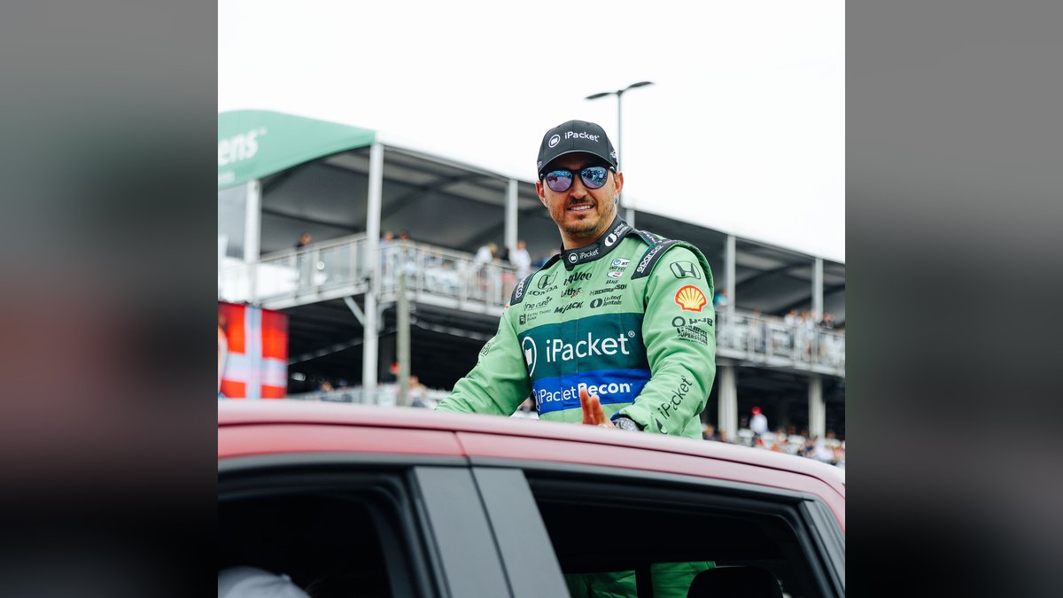 Graham Rahal smiling in a green IndyCar firesuit and headset at Detroit