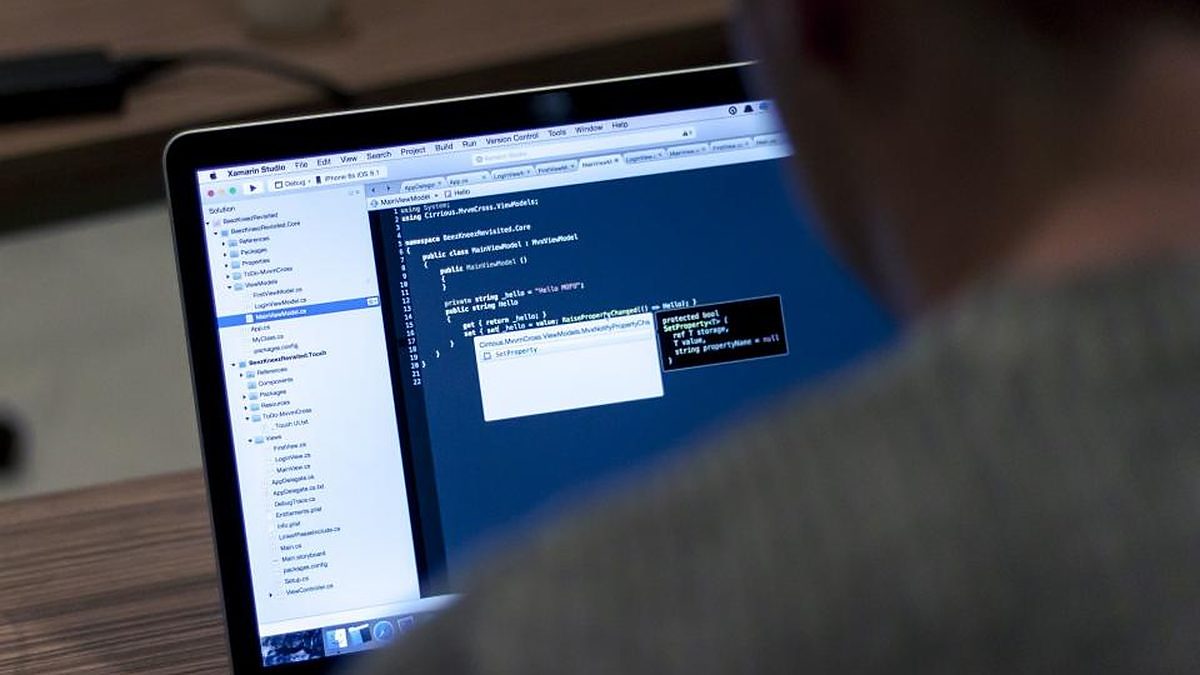A software developer writes code on a laptop at a desk