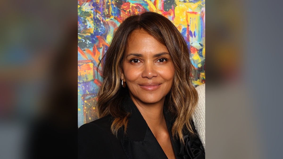 Halle Berry smiling in a black blazer in front of a colorful painting