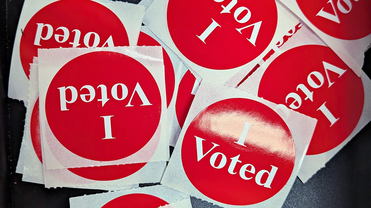 A pile of round red and white I Voted stickers scattered across a table at a polling place