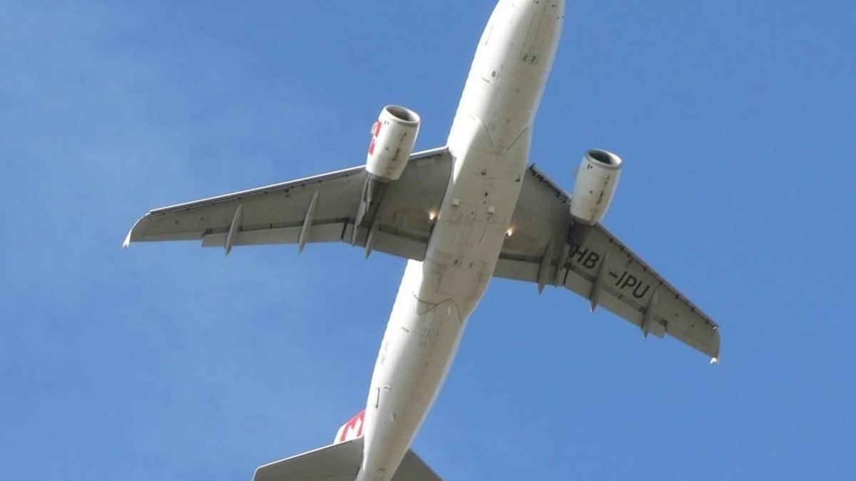 A white passenger jet climbs overhead against a clear blue sky just after takeoff with its landing gear still down