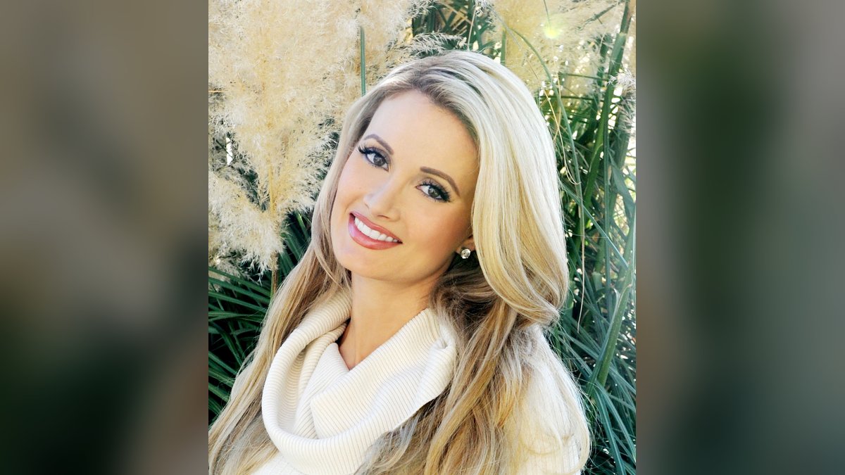 Holly Madison smiling in a cream turtleneck in front of tall grasses