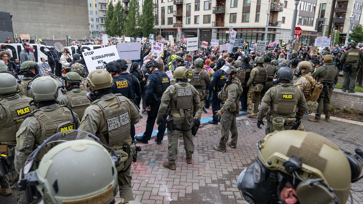 Federal officers in tactical gear facing protesters on a city street