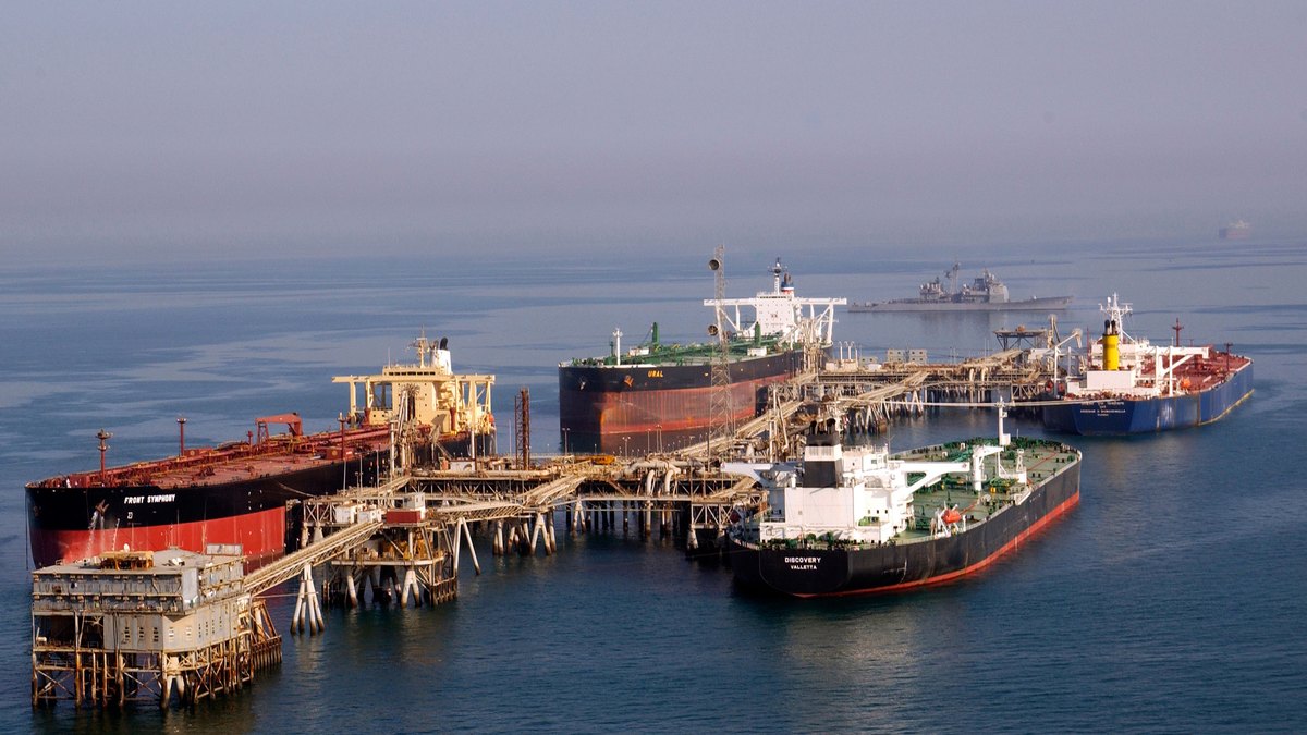 Four large oil tankers moored at an offshore oil terminal in the Persian Gulf with a U.S. Navy warship on the horizon