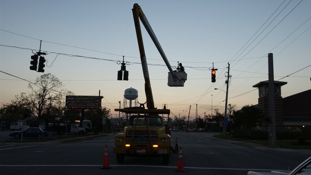 A utility crew in a bucket truck repairing power lines over a Pensacola street at dusk