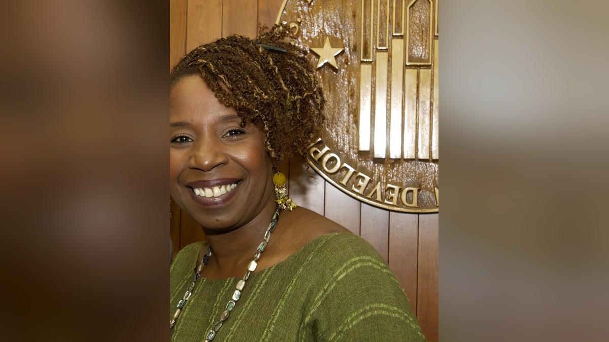 Iyanla Vanzant smiling in a green top and long beaded necklace in front of a wood-paneled wall