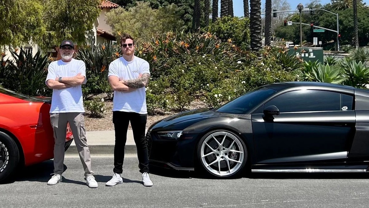 James Wehr in sunglasses and a white T-shirt standing beside his father and a black sports car