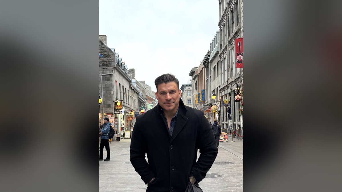 Jax Taylor in a dark coat standing on a cobblestone street