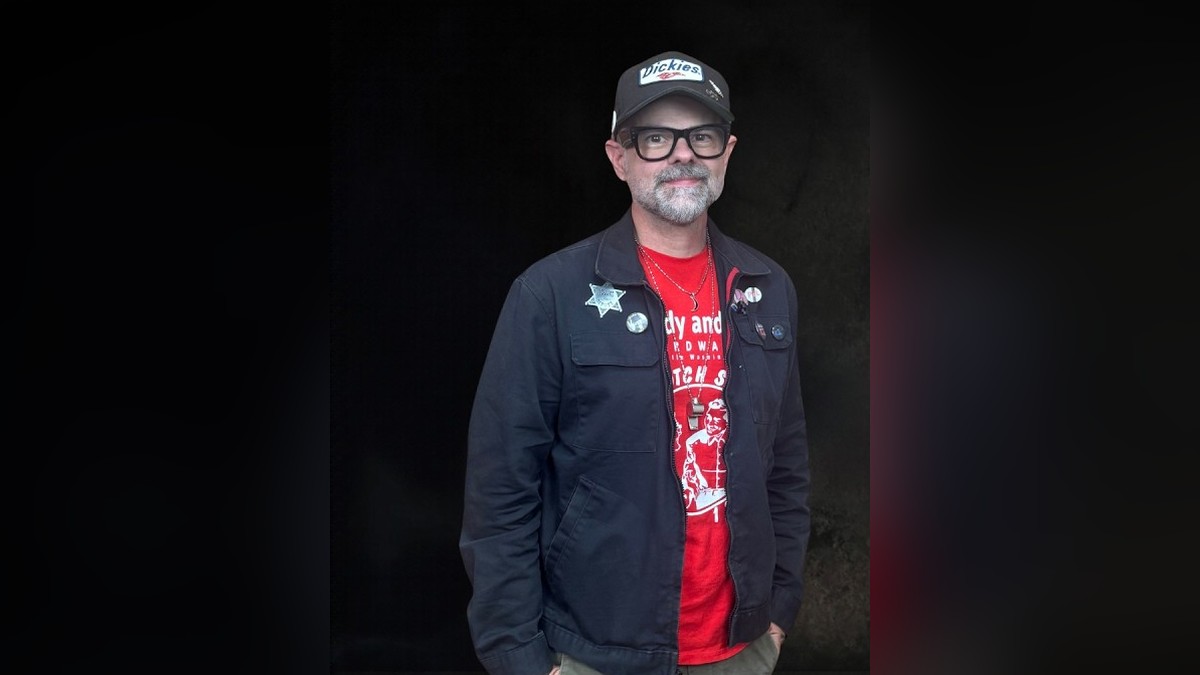 Jay Bakker in a black cap and glasses wearing a navy jacket over a red T-shirt