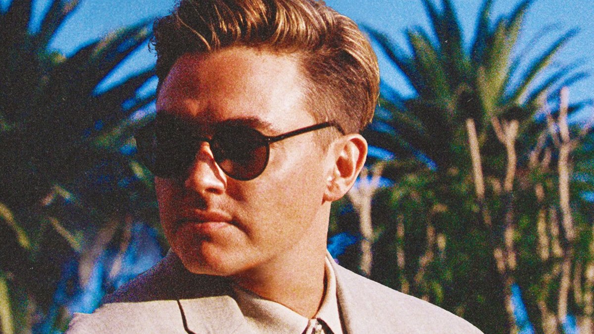 Jesse McCartney in sunglasses and a light blazer in front of palm trees