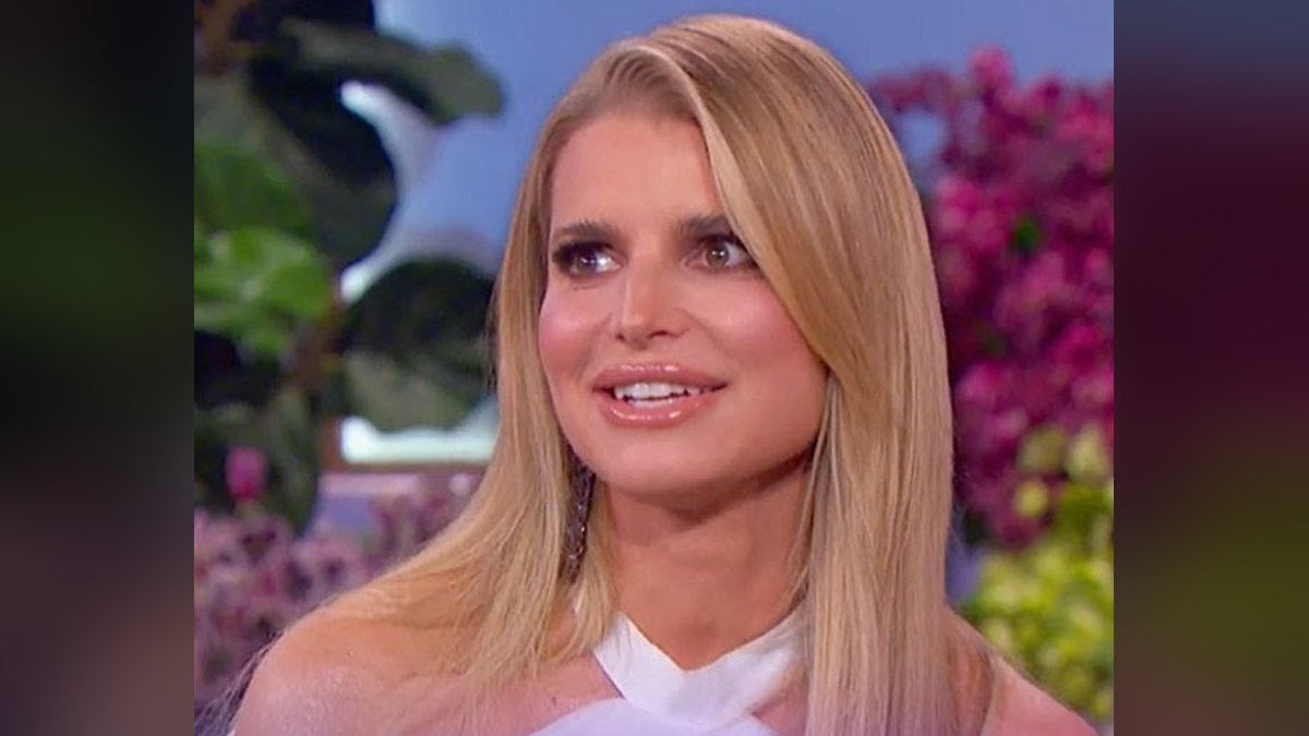 Jessica Simpson smiling with long blond hair in a white halter top in front of pink flowers