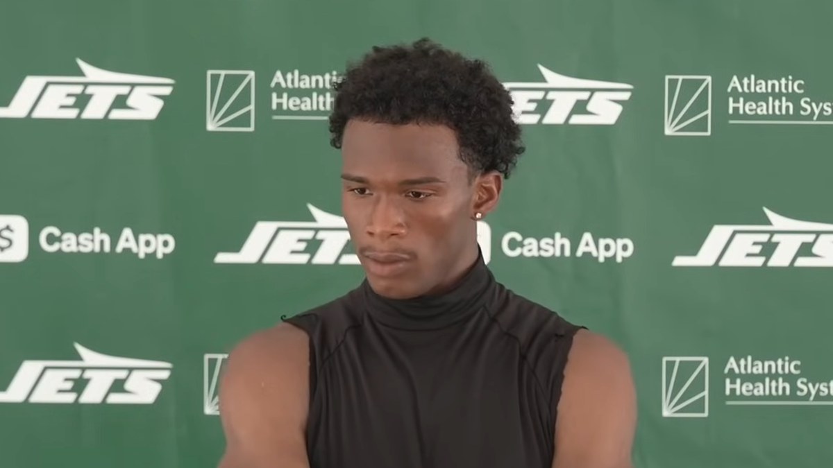 Garrett Wilson in a black sleeveless turtleneck at a Jets training camp press conference in front of a green Jets backdrop
