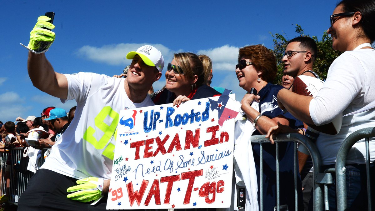 J.J. Watt in a Pro Bowl jersey and cap taking a selfie with smiling Texans fans holding a WATT-age sign in 2014