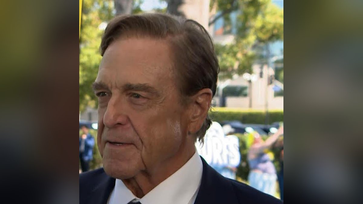 John Goodman in a navy suit and tie at an outdoor event