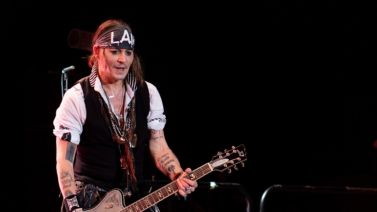 Johnny Depp grinning onstage with an electric guitar under a bandana