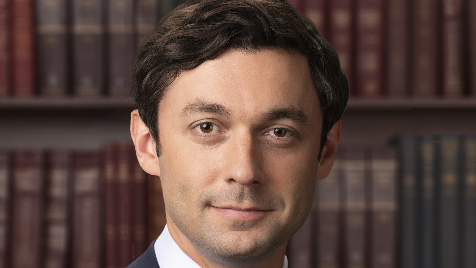 Official US Senate portrait of Georgia Sen. Jon Ossoff smiling in front of shelves of law books