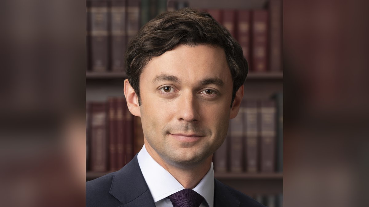 Official Senate portrait of Jon Ossoff in a dark suit and purple tie in front of shelves of law books