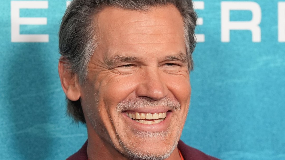 Josh Brolin smiling in a maroon blazer at a movie premiere backdrop