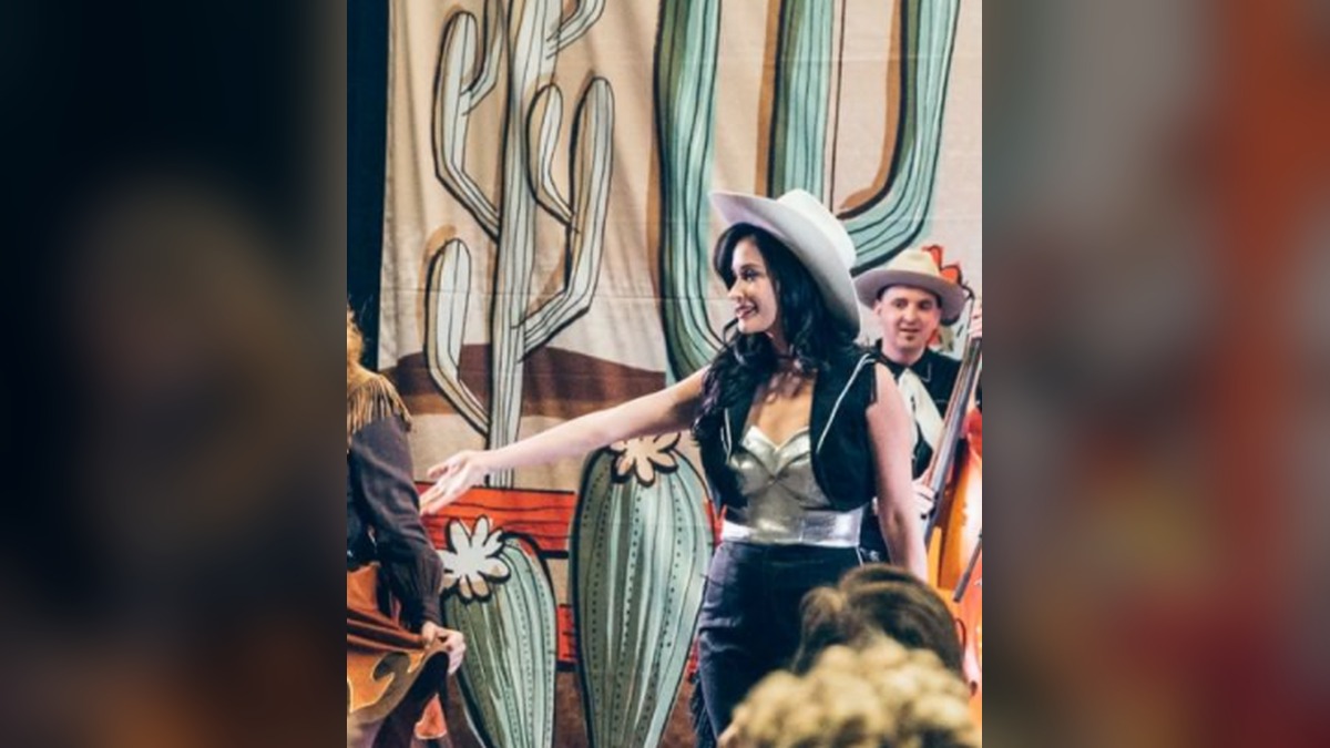 Kacey Musgraves in a white cowboy hat on a stage decorated with painted cactuses
