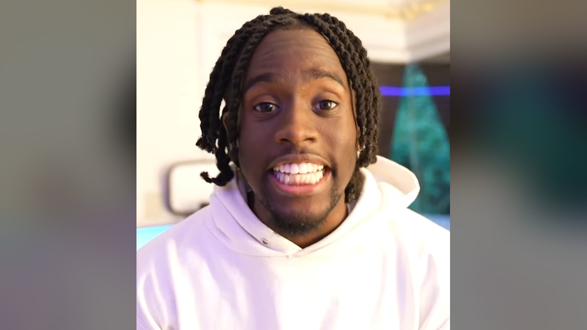 Kai Cenat smiling in a white hoodie