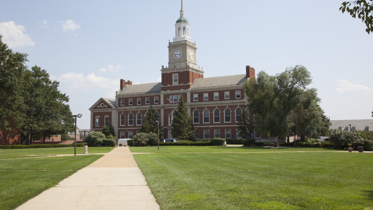 A paved walkway crosses a green lawn toward Founders Library and its white clock tower at Howard University