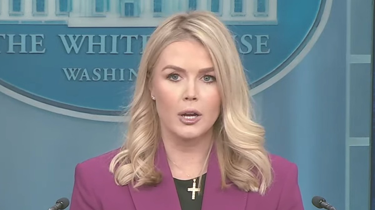 Karoline Leavitt with shoulder-length blond hair in a magenta blazer speaking at the White House briefing room podium