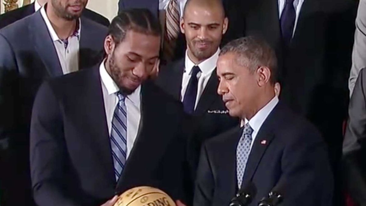 Kawhi Leonard in a suit handing a basketball to President Barack Obama at the Spurs' 2015 White House visit