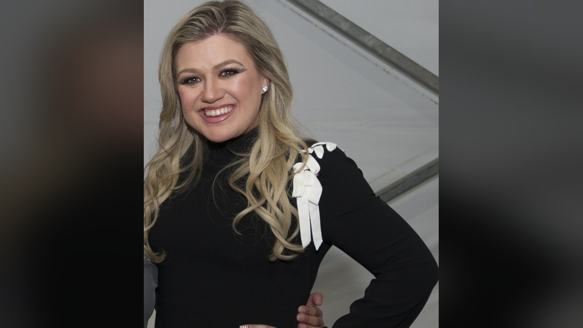 Kelly Clarkson smiling in a black dress with white bow trim at the 2018 Warrior Games
